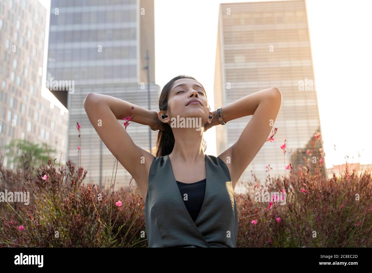 Relaxed young businesswoman listening music through earphones with hands behind head against office building during break Stock Photo