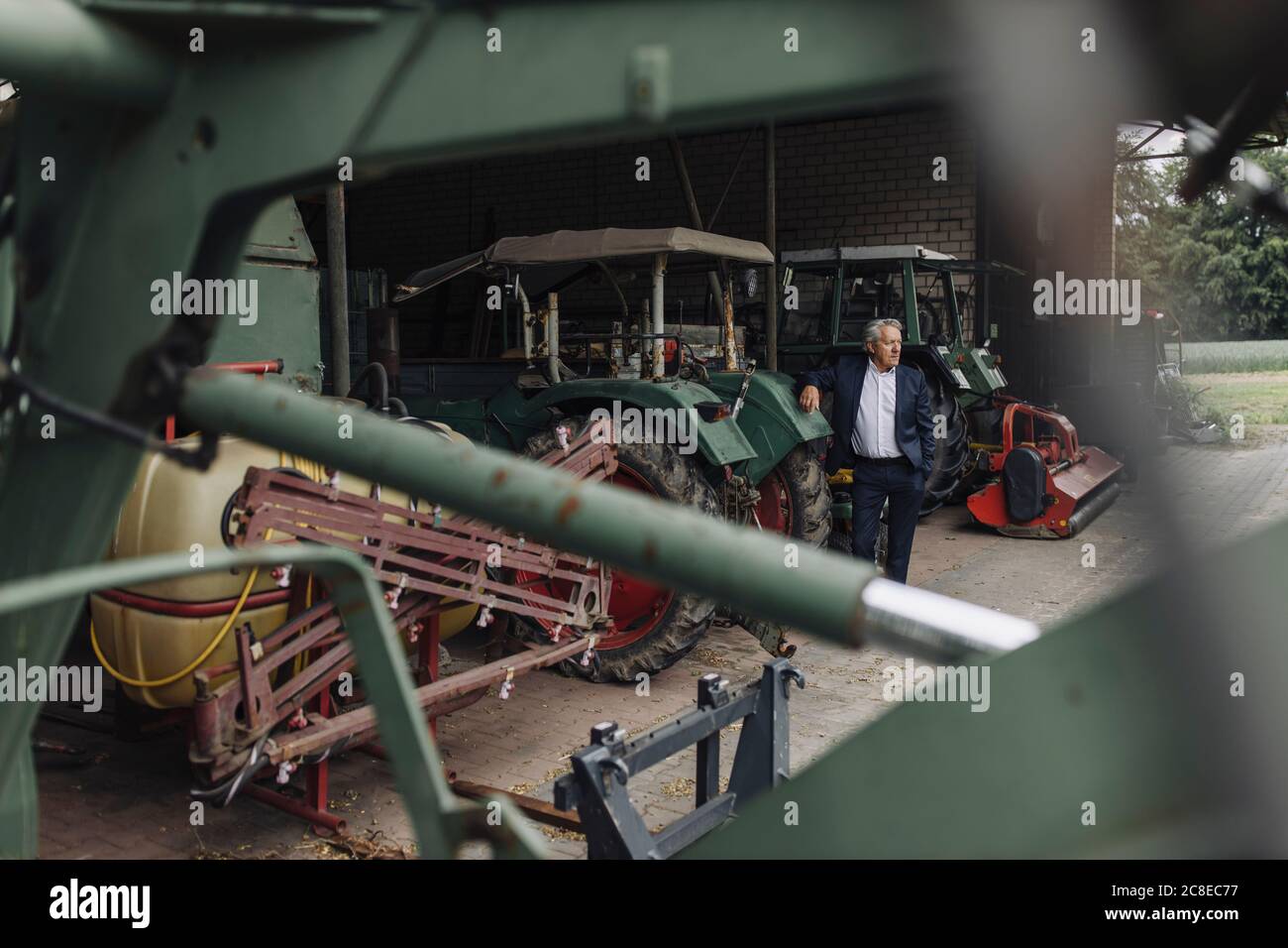 Senior businessman on a farm with tractor in barn Stock Photo