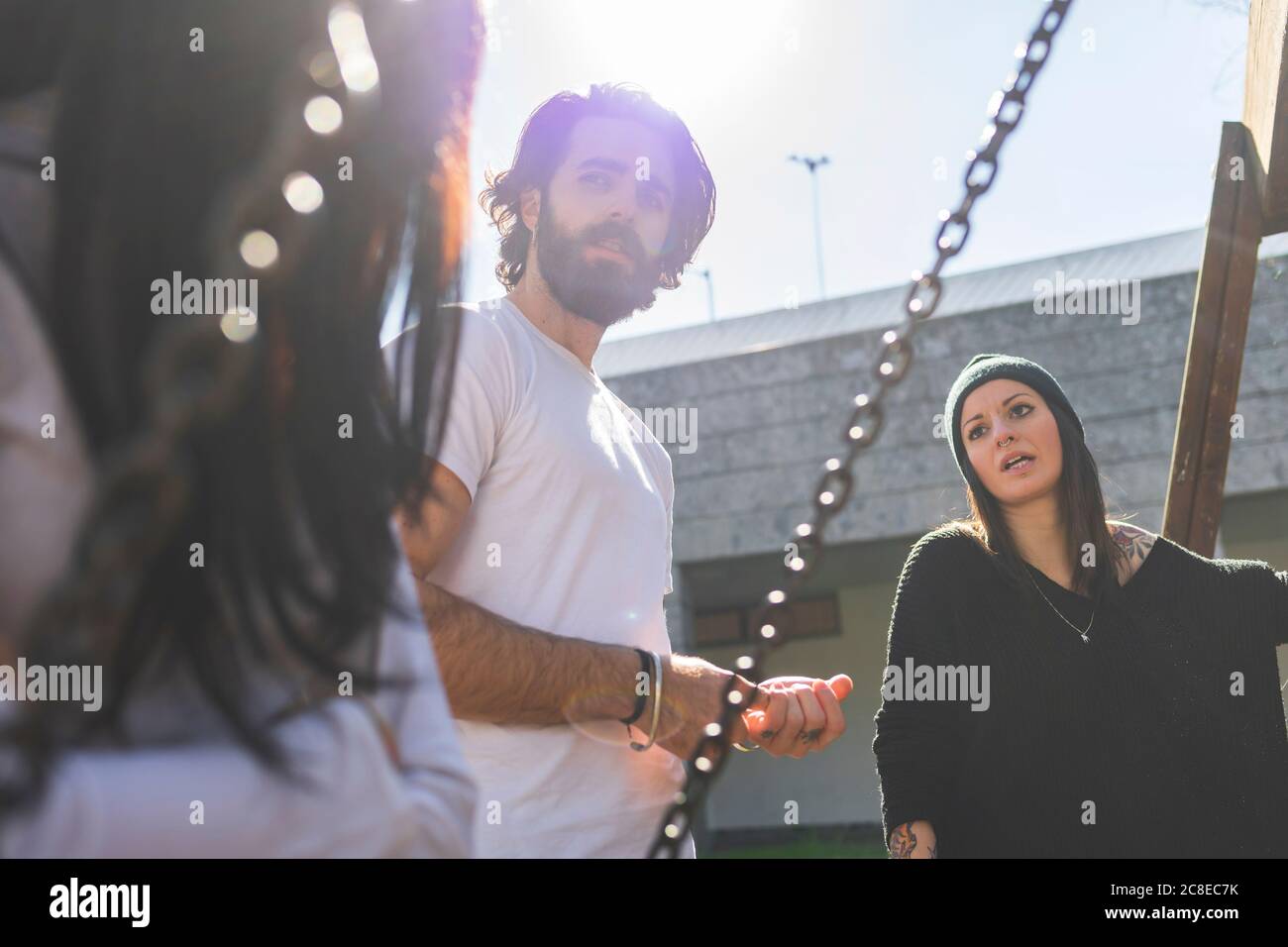 Young man talking with female friends while standing against clear sky on sunny day Stock Photo
