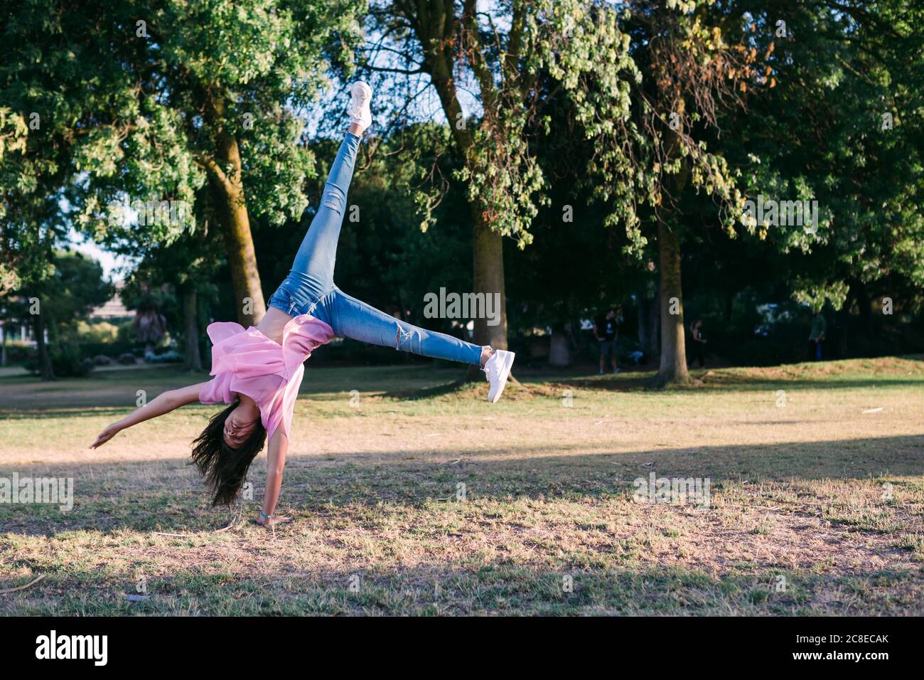 Girl doing cartwheel on land against trees in park Stock Photo