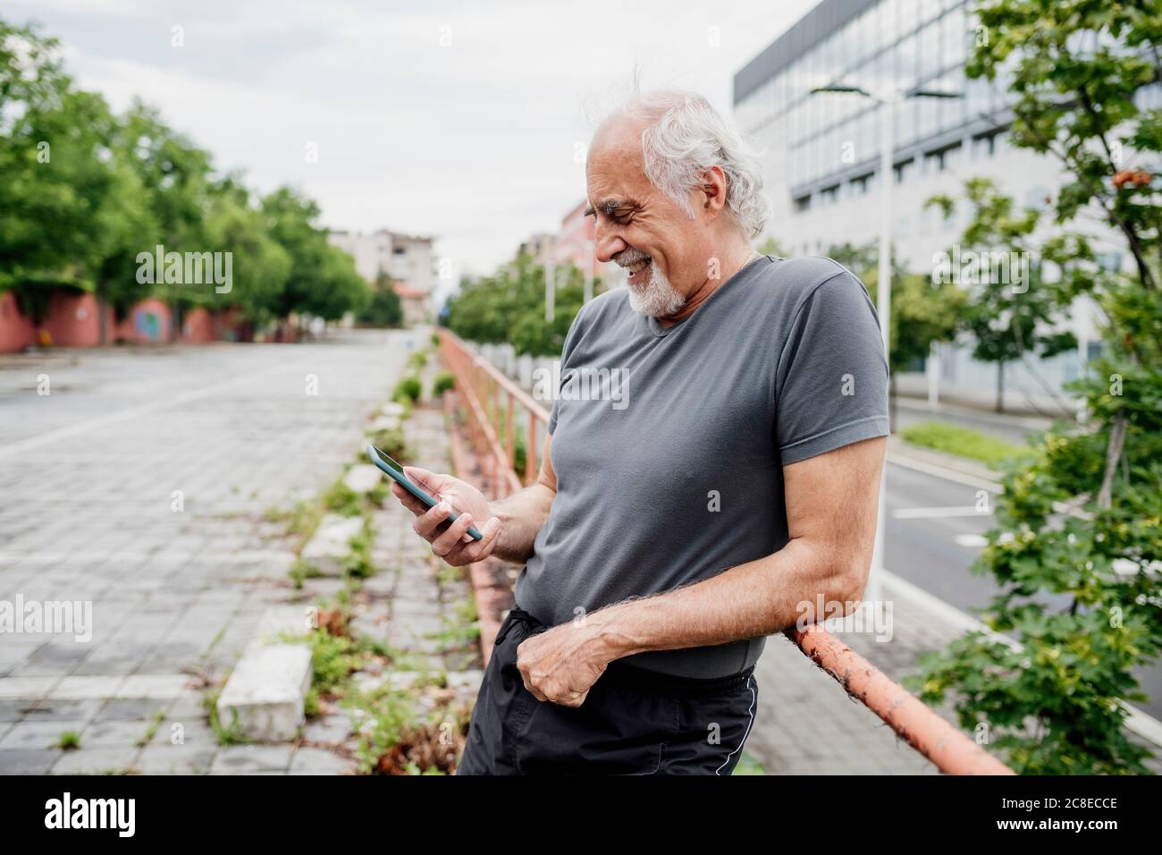 Smiling senior man using smart phone while standing by railing in city Stock Photo