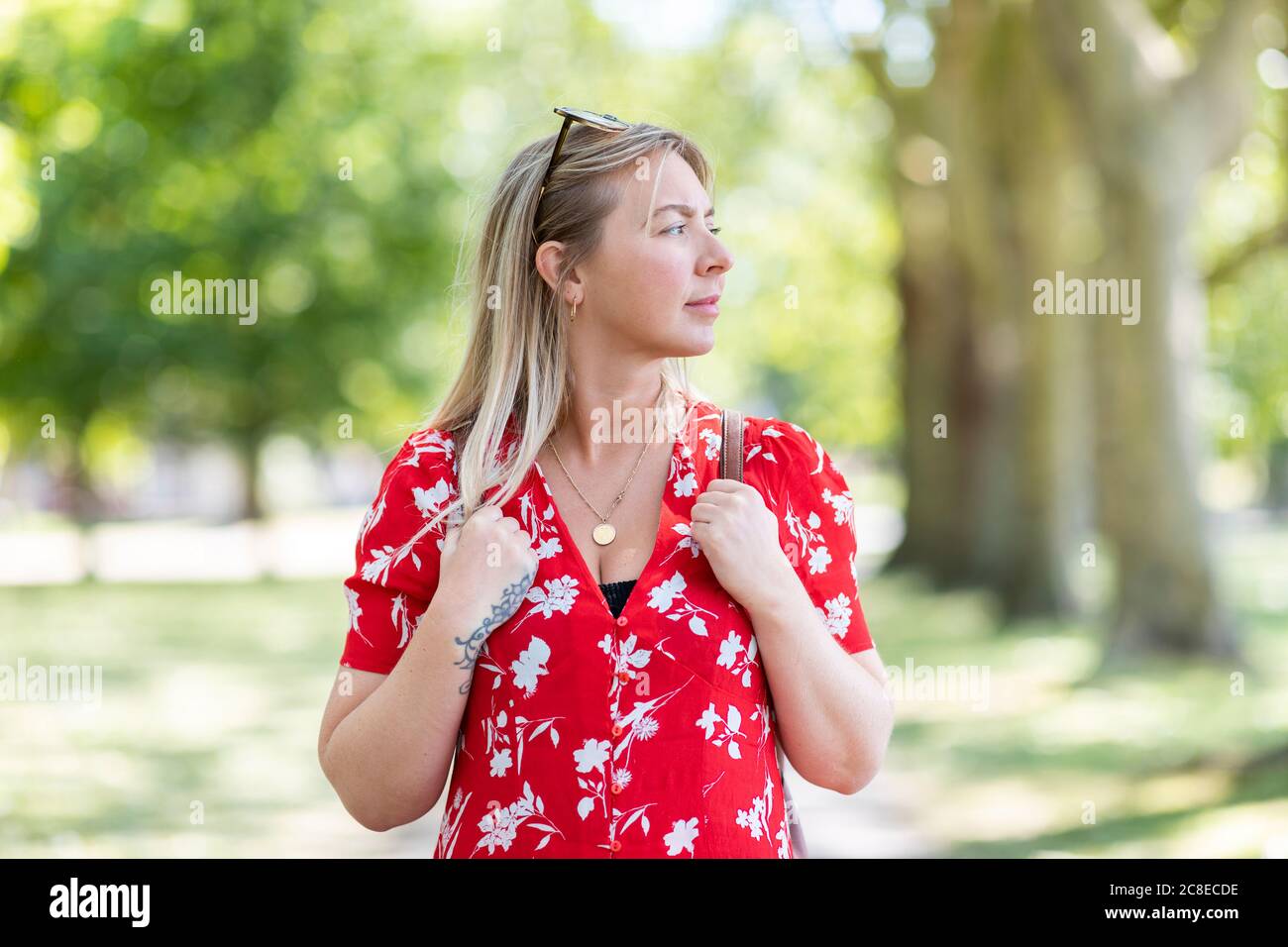 Thoughtful woman standing in public park during sunny day Stock Photo