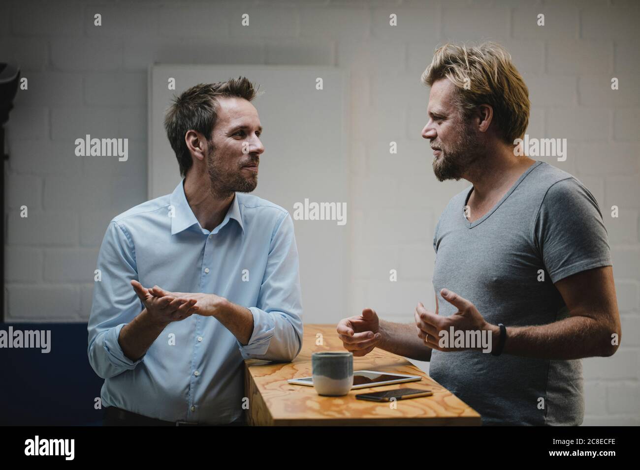 Two casual businessmen discussing in office with portable devices on counter Stock Photo