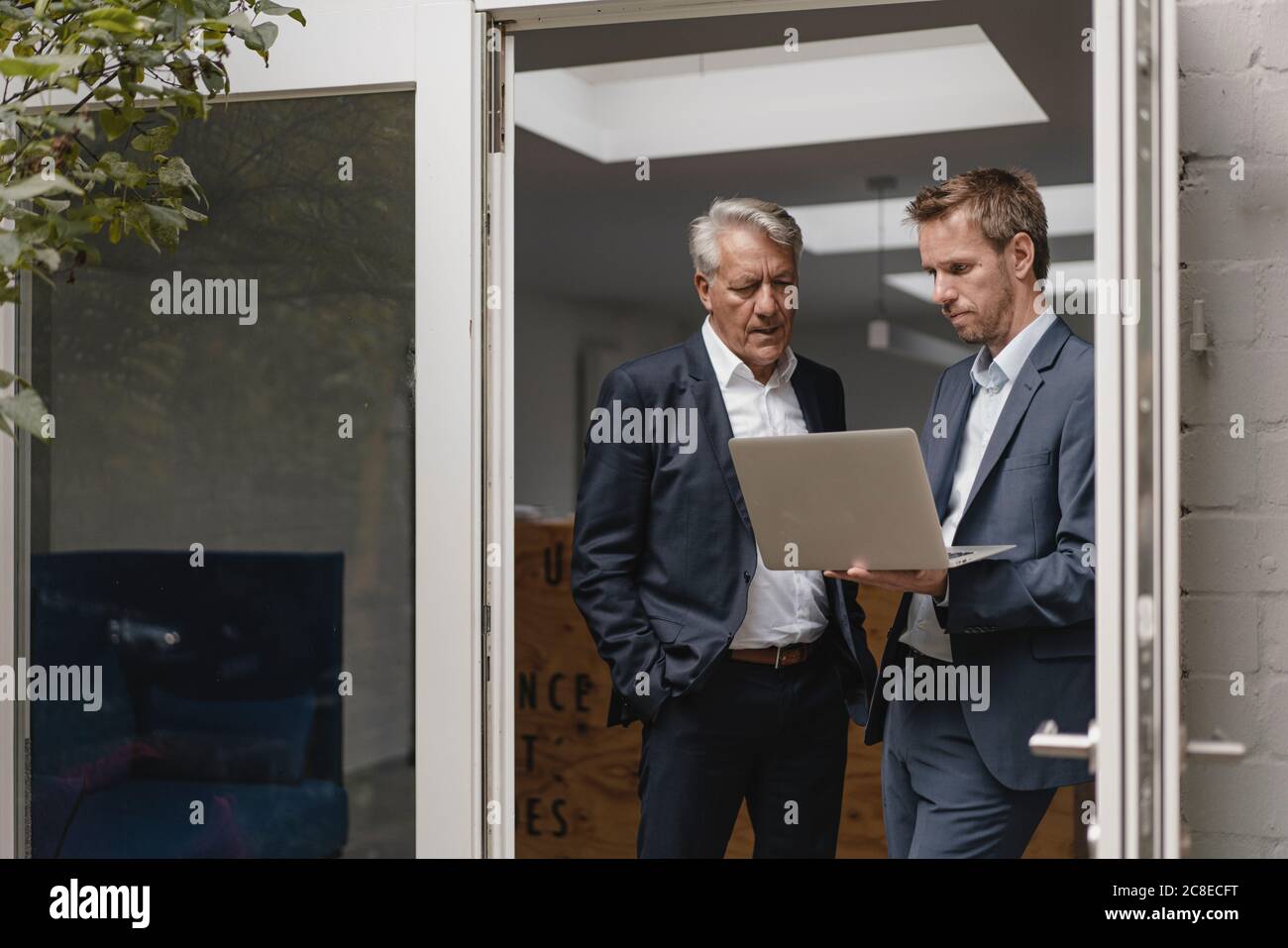 Two confident businessmen using laptop, standing in office door Stock Photo