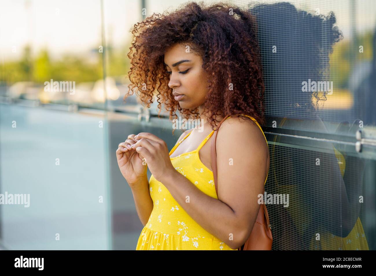 Young woman with afro hair wearing yellow dress standing by modern wall in city Stock Photo