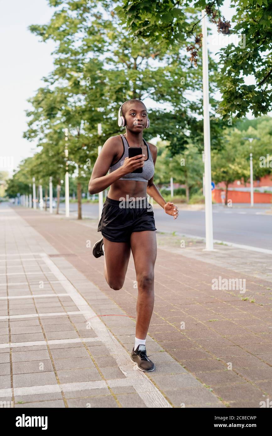 Female athlete listening music while running on footpath in city