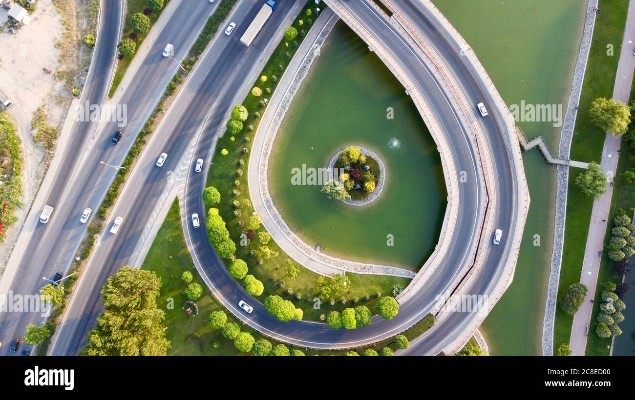 Aerial view of the roundabout on the river. Trees, overpass, buildings and vehicles can be seen. Stock Photo