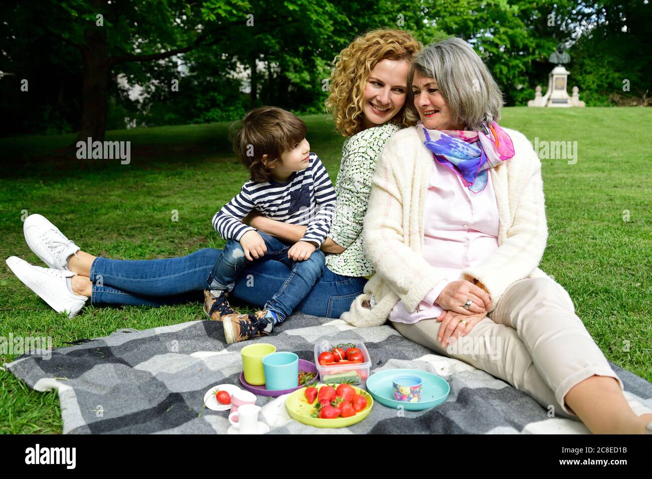 Happy boy enjoying picnic with mother and grandmother at public park Stock Photo