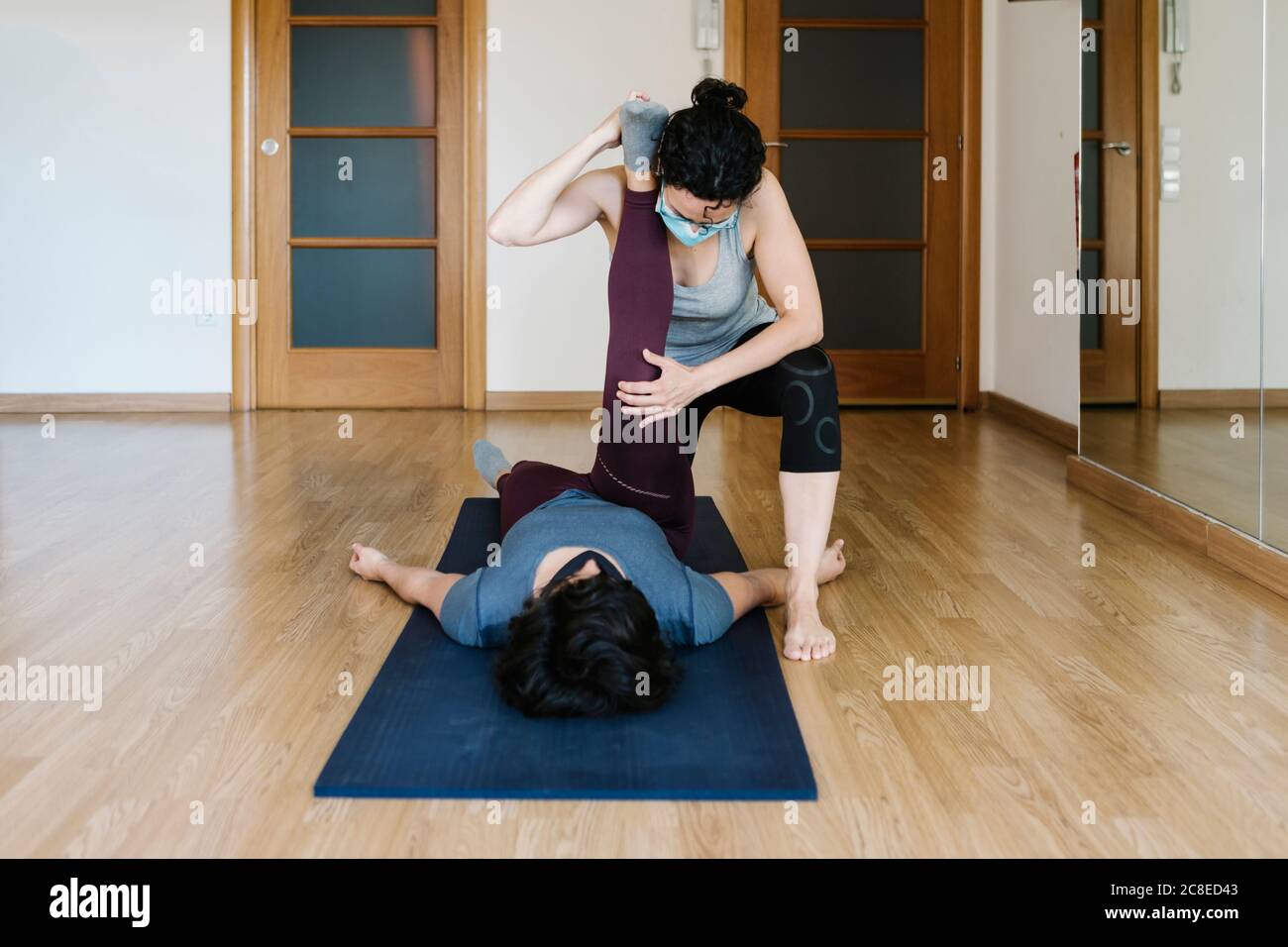 Physiotherapist wearing mask stretching patient's leg lying on exercise mat Stock Photo