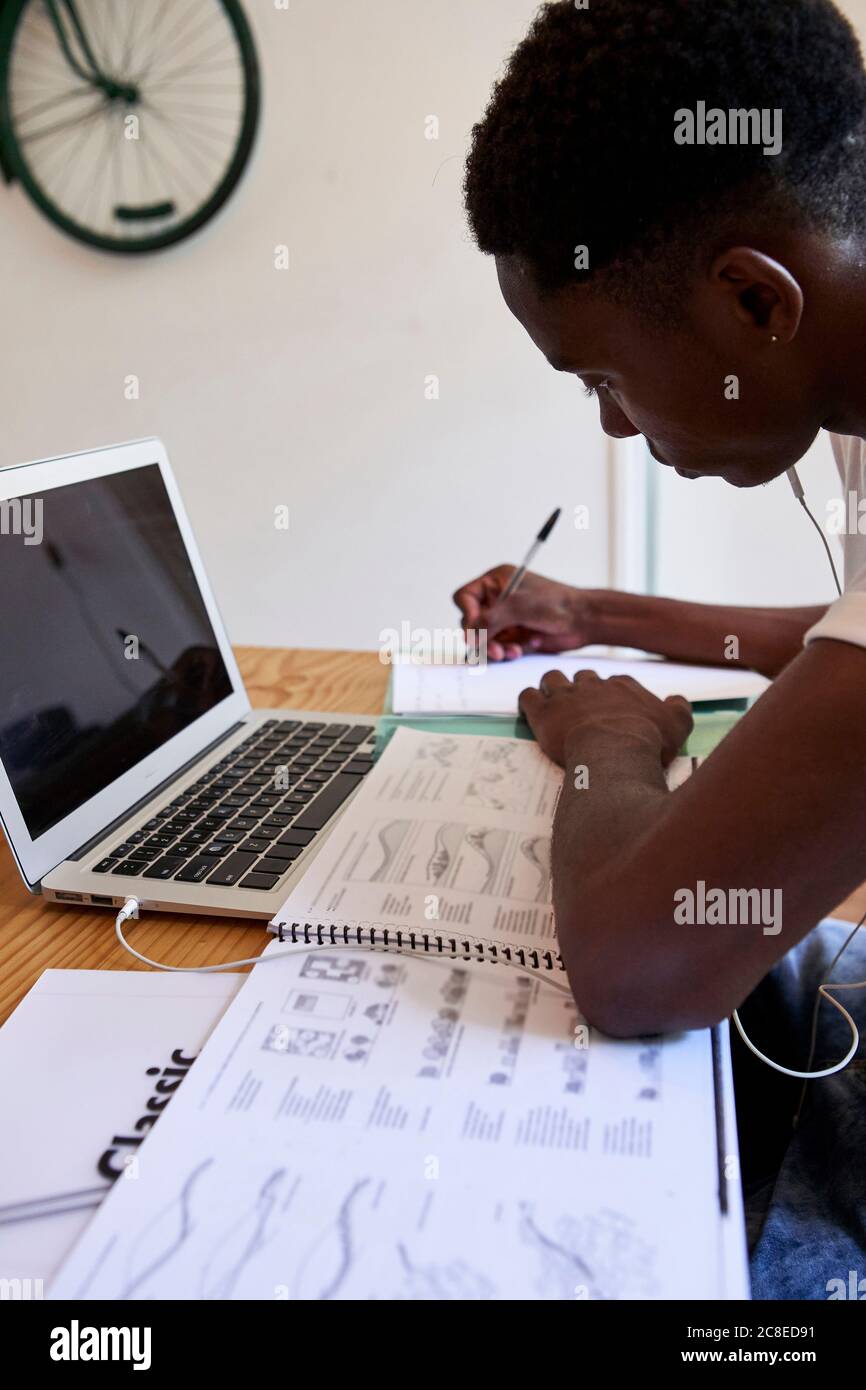 Focused young man writing notes in book while sitting at home Stock Photo