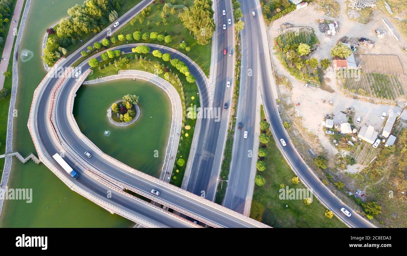 Aerial view of the roundabout on the river. Trees, overpass, buildings and vehicles can be seen. Stock Photo