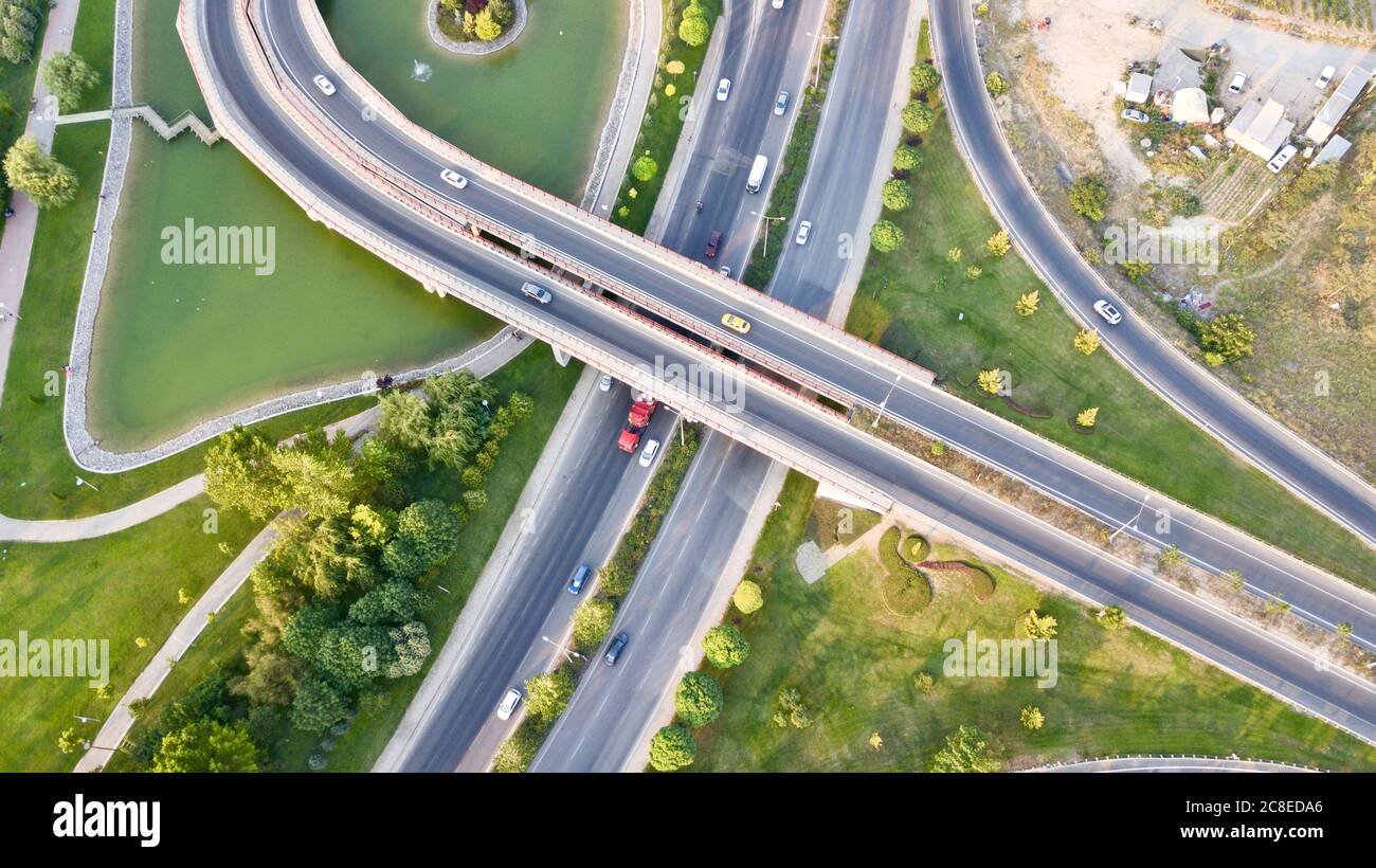Aerial view of the roundabout on the river. Trees, overpass, buildings and vehicles can be seen. Stock Photo