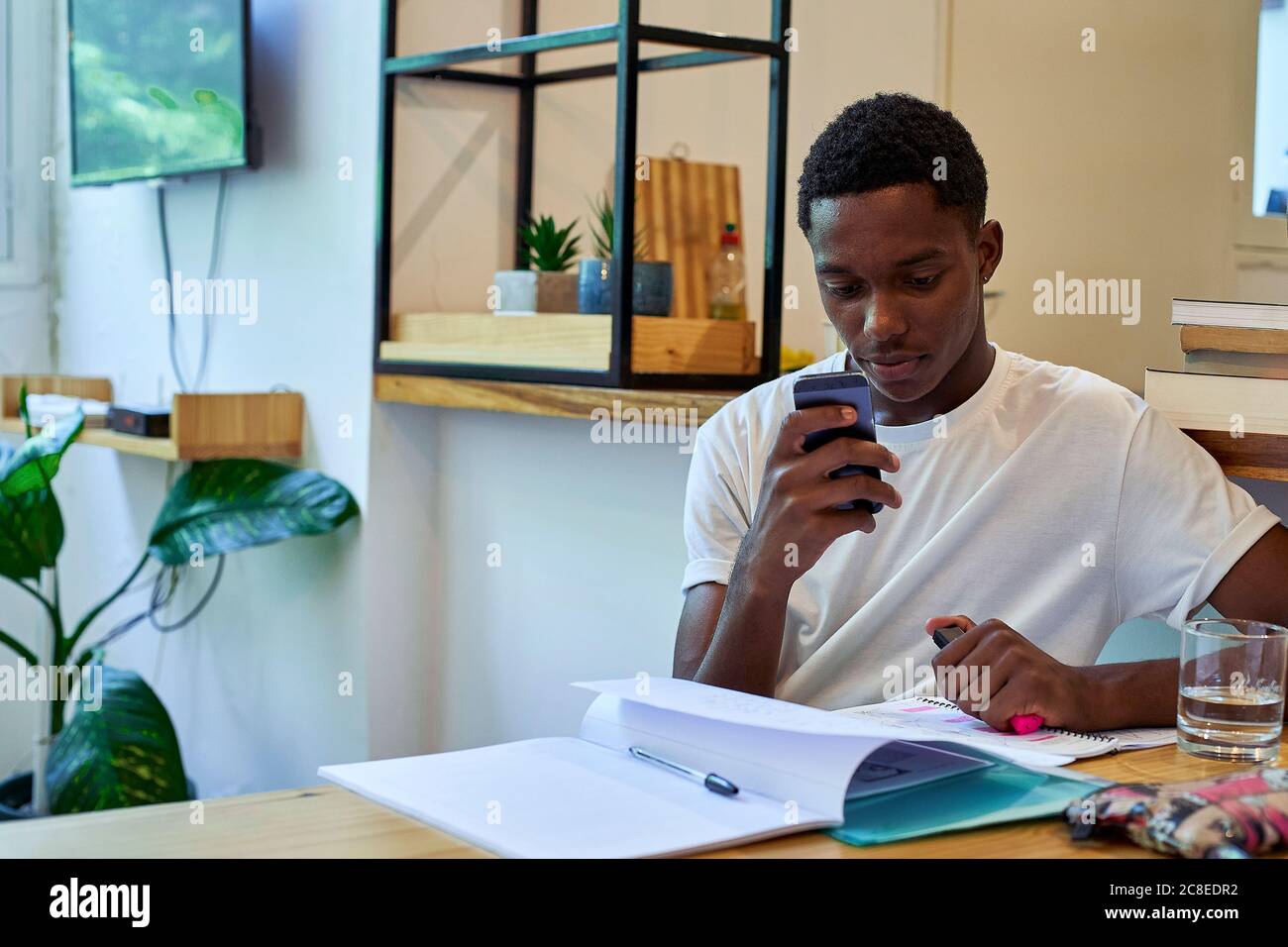 Young man using smart phone while studying on table at home Stock Photo