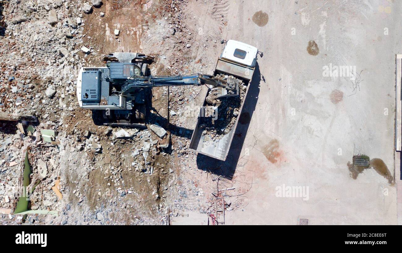 Aerial view of excavator demolishes an old building in city center. Destroyed concrete is loaded on the truck Stock Photo