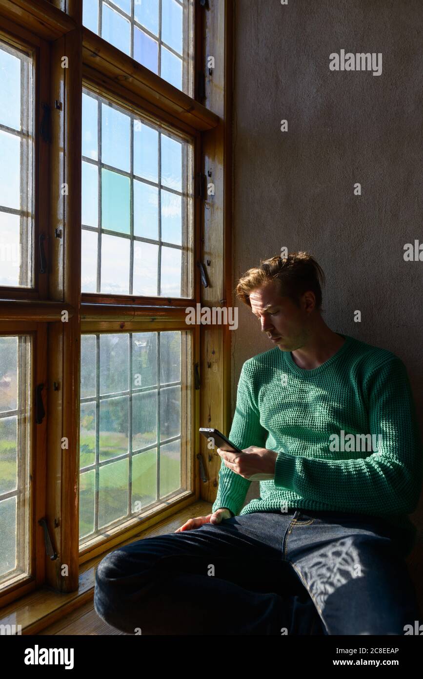 Young handsome man using mobile phone in front of closed wooden window Stock Photo