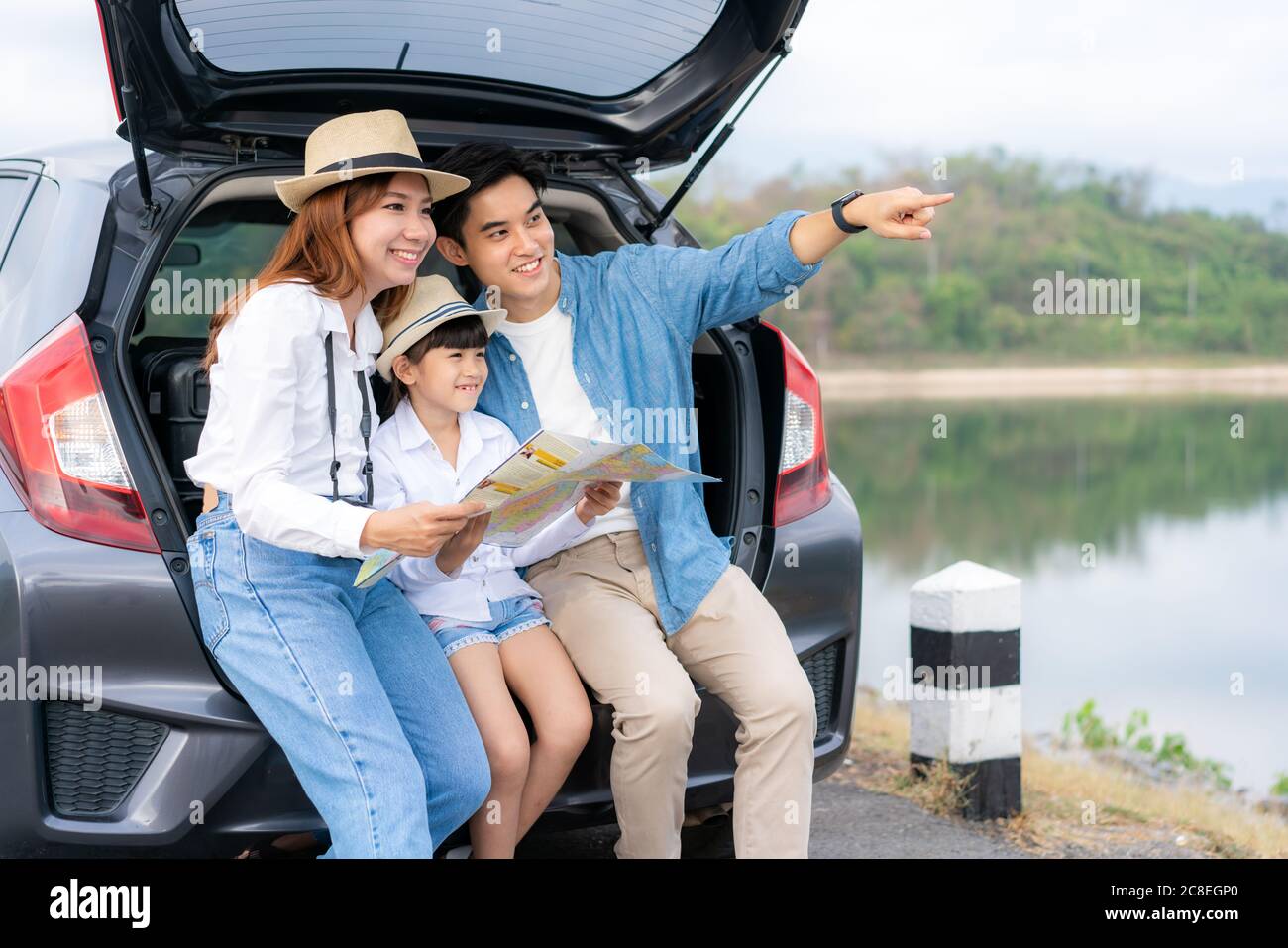 Portrait of Asian family sitting in car with father pointing to view and mother with daughter looking beautiful landscape and holding maps while vacat Stock Photo