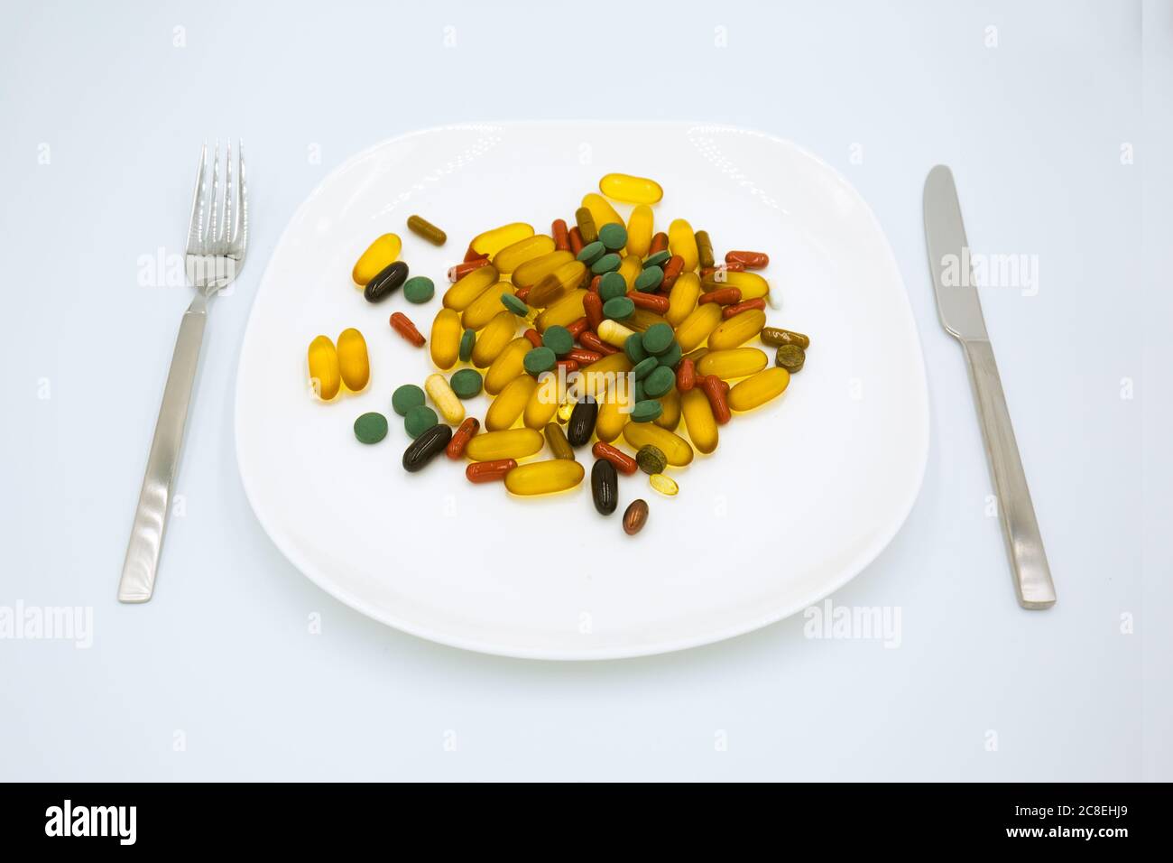 Many different weight loss pills and supplements as food on white plate with fork and knife. Diet pills and supplements, prescription weight loss drug Stock Photo
