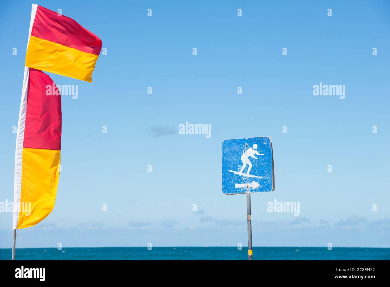 Red and yellow coloured flags of  surf live savers and surfing sign at Australian beach, with ocean and sky in blurred background and copy space. Stock Photo