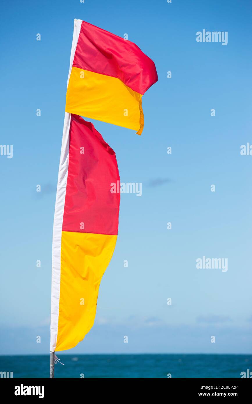 Red and yellow coloured flags of  surf live savers at Australian beach, with ocean and sky as blurred background. Stock Photo
