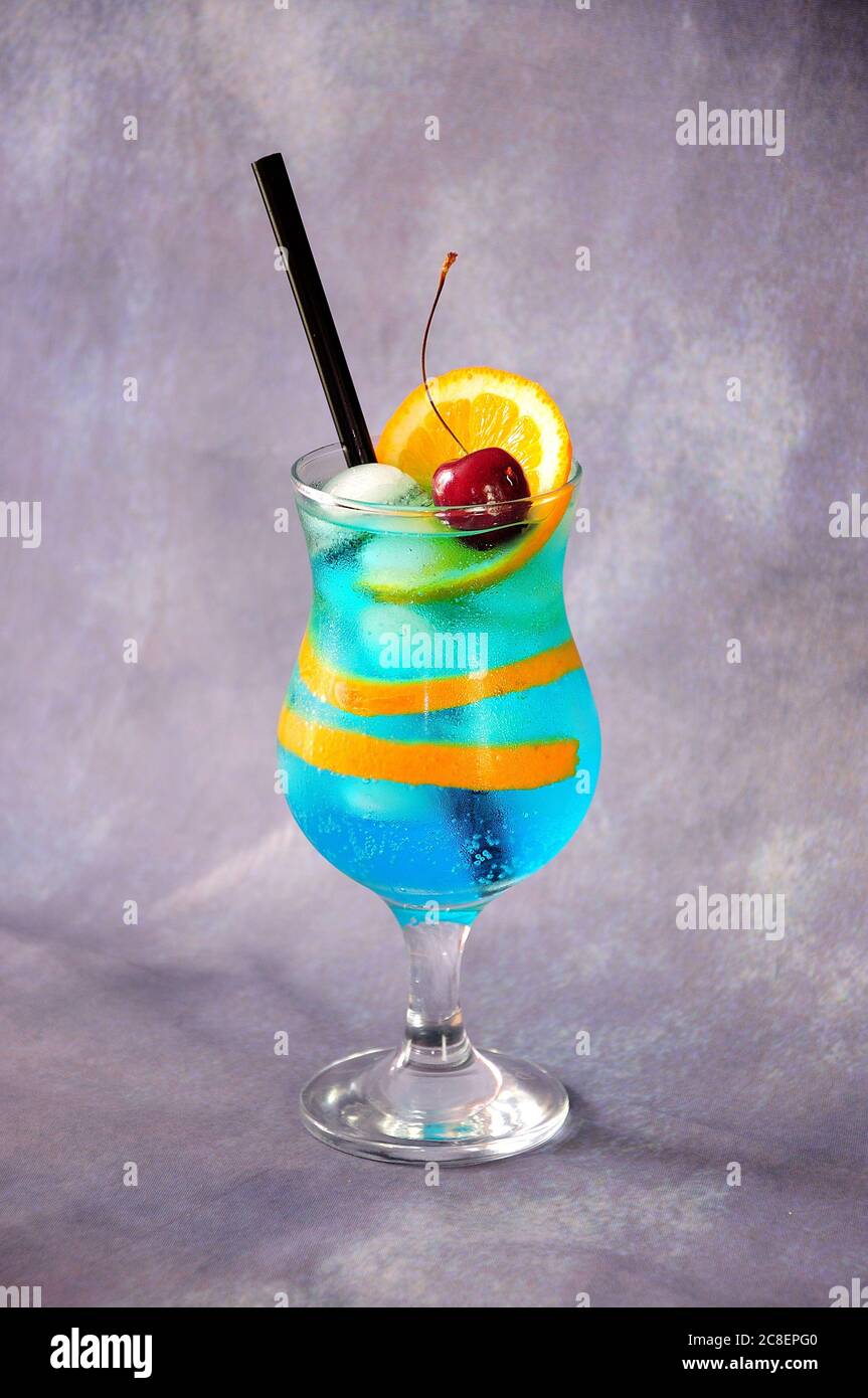 Tall glass with blue lagoon cocktail with zest and orange slice, ripe ...