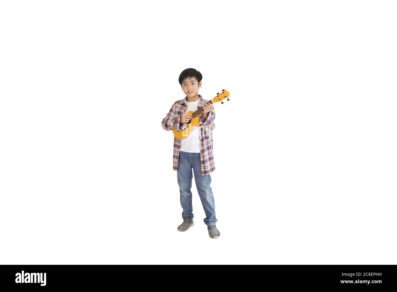 A portrait of a cute Asian elementary school student wearing jeans and wearing a plaid shirt holding a ukulele. An isolated image with white backgroun Stock Photo