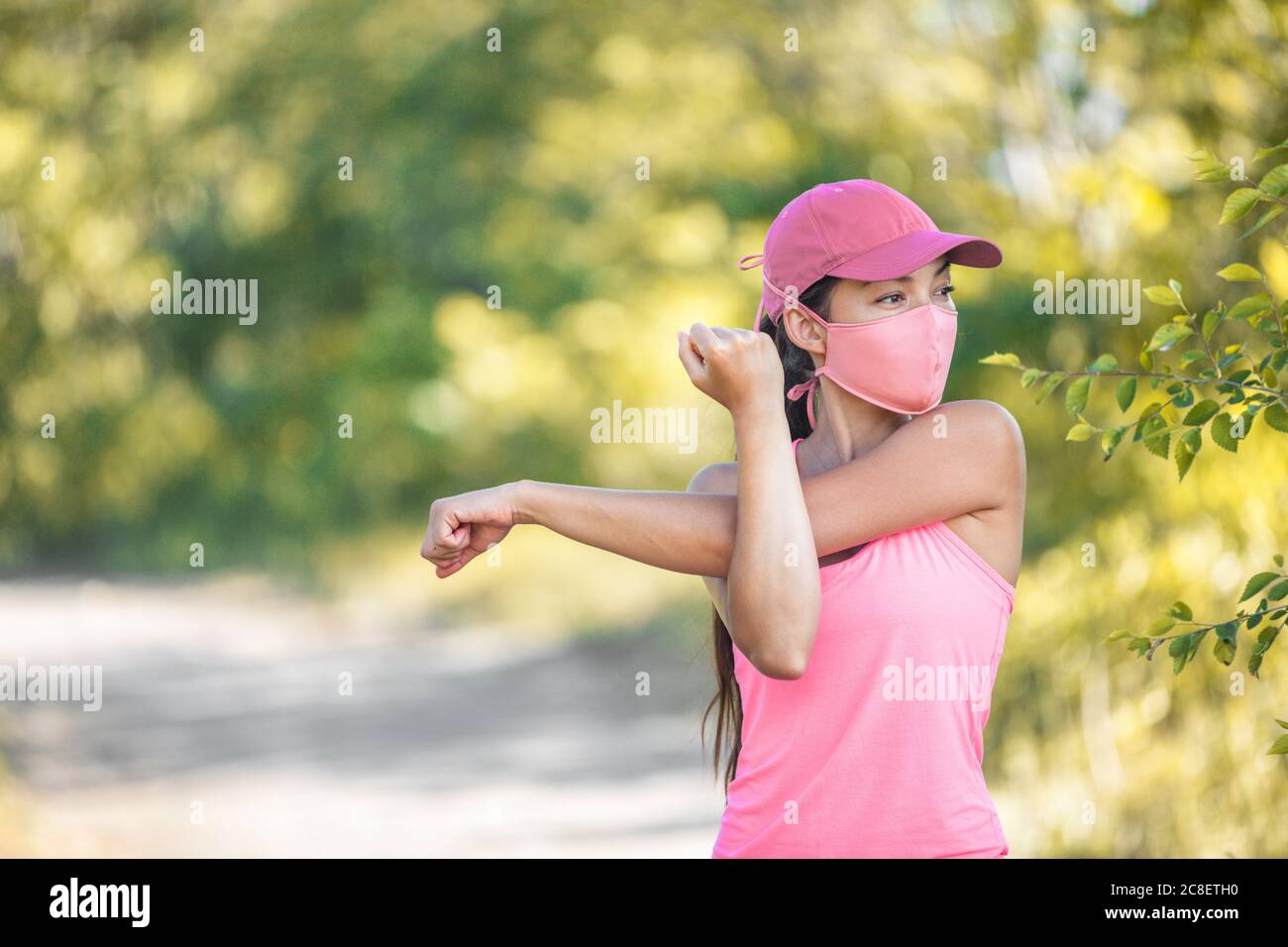 Mask covid-19 runner woman stretching arms before cardio workout on outdoor summer park run jogging wearing face covering protection for coronavirus Stock Photo