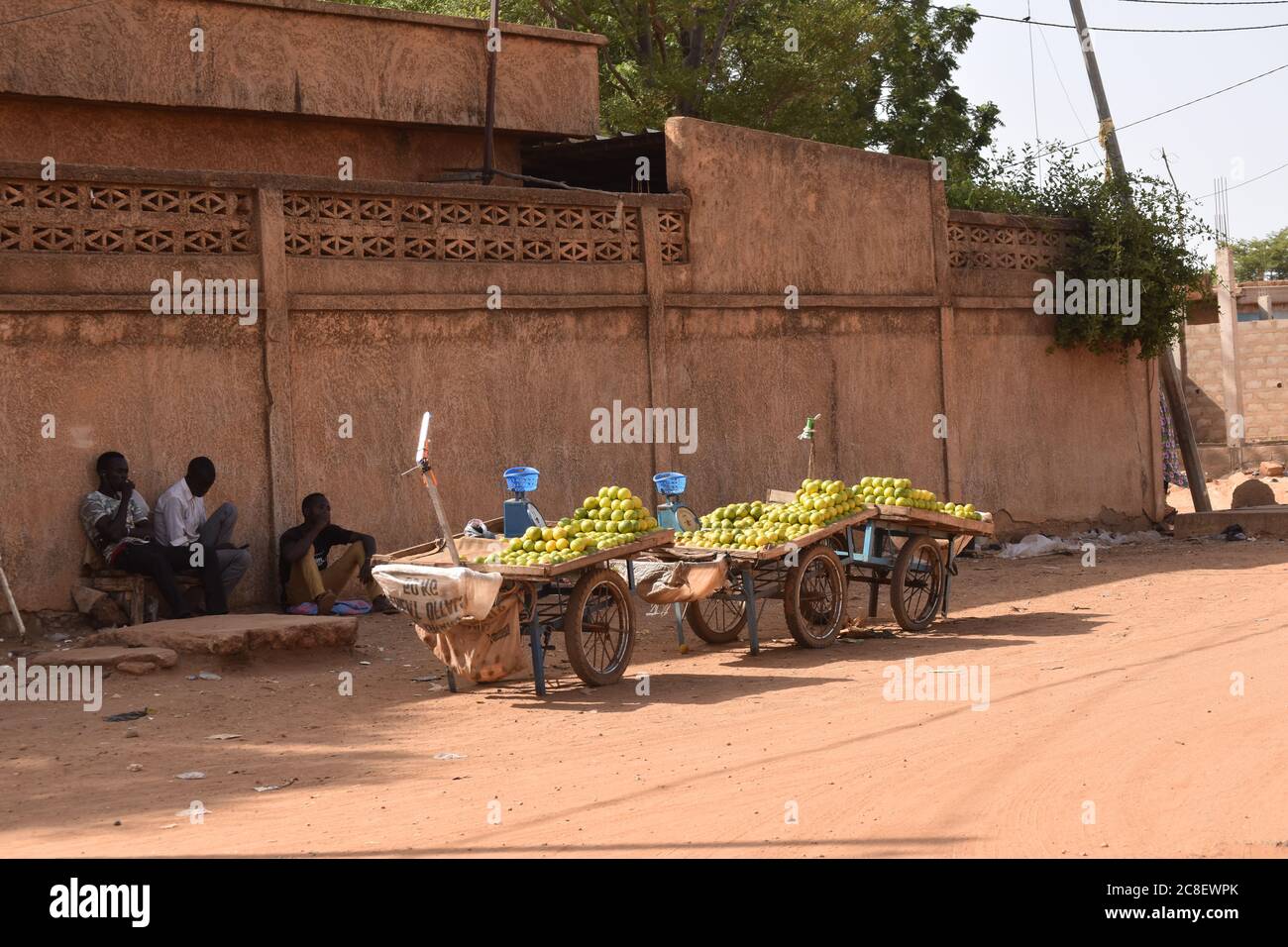 Three push carts loaded with oranges for sale sit on the side of a road while their owners rest in the shade, in Niamey, Niger, Africa. Stock Photo