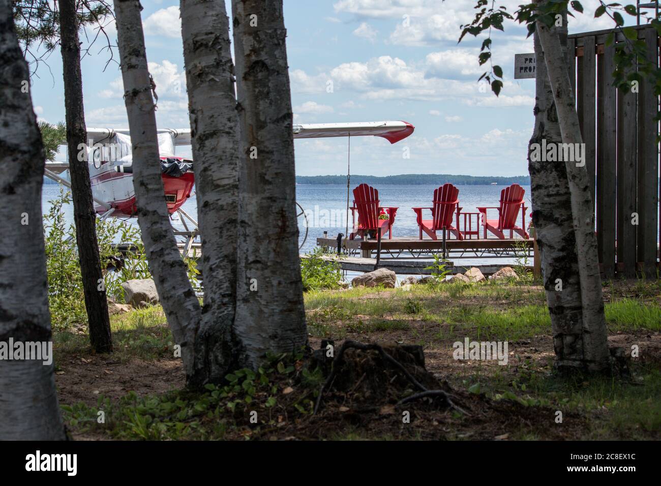 Three red Muskoka chairs on a dock looking out into the lake Stock