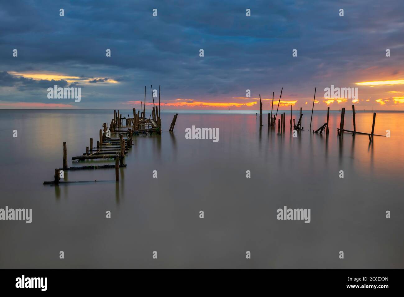 Morning scenery with rain clouds in the sky and golden light from the sun at a fishing village with an old, broken wooden bridge. Stock Photo