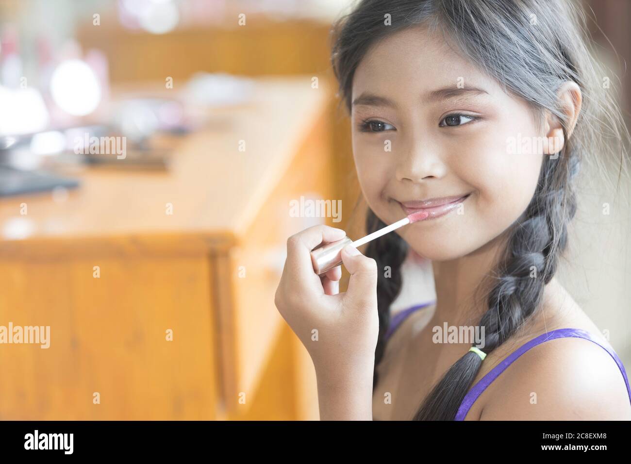 A cute long-haired Asian schoolgirl is using lipstick to apply lip makeup during a makeup lesson. Stock Photo