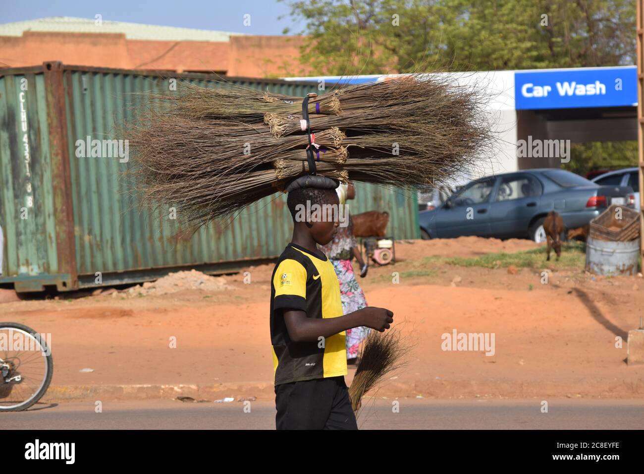 A mobile vendor balances his load of handmade straw brooms on his head. Stock Photo