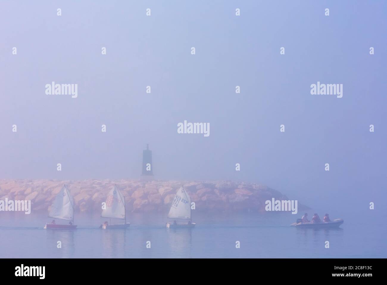 Three Optimist dinghies being towed from port in early morning sea mist, Marbella, Costa del Sol, Malaga Province, Spain. Stock Photo