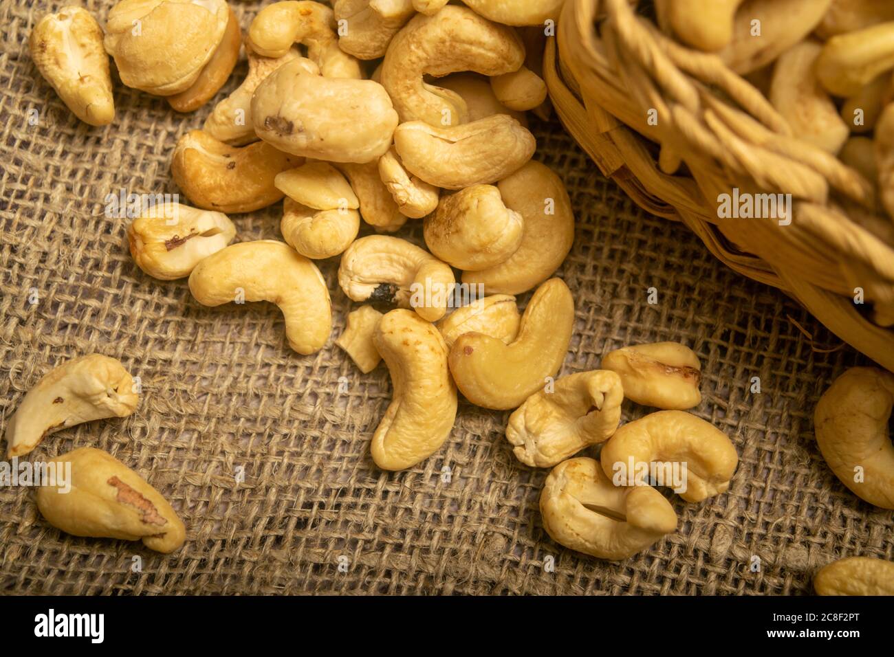 Cashew nuts in a wicker basket and cashew nuts scattered on burlap with a rough texture surface texture. Close up Stock Photo