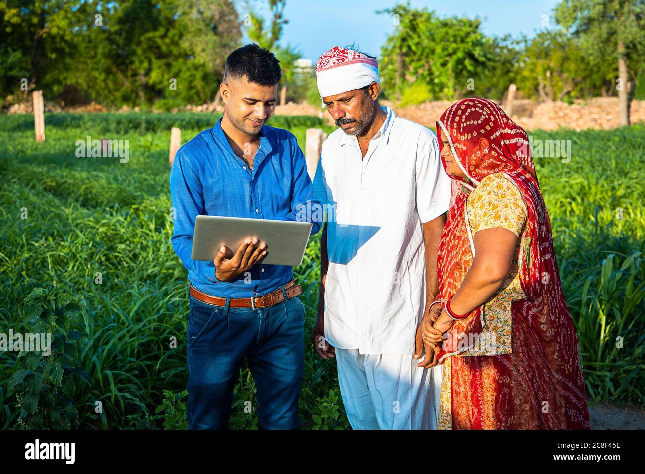 Young indian man with laptop showing something to village farmer family