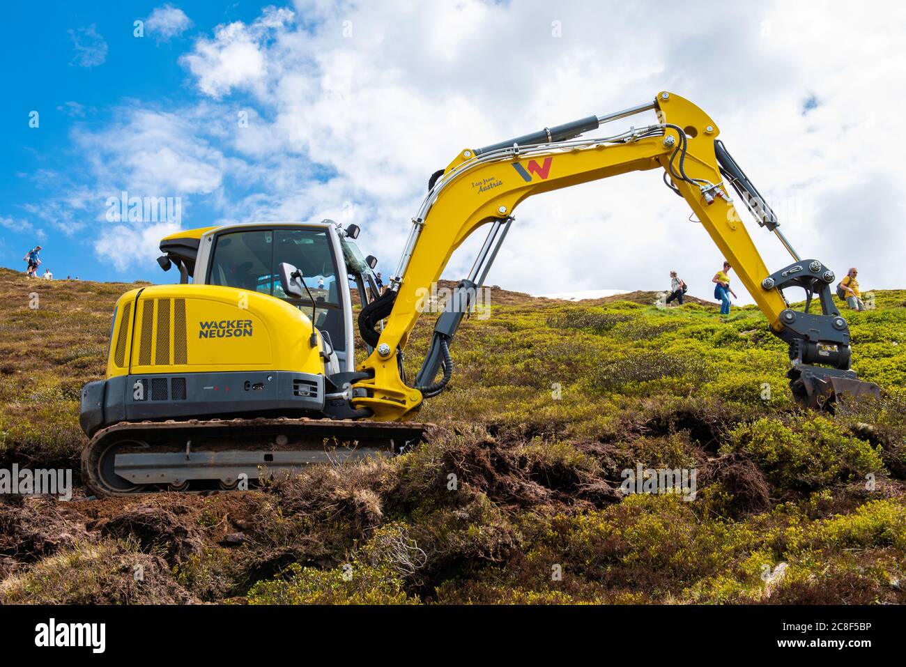 MAYRHOFEN, AUSTRIA - Jun 22, 2019: small yellow excavator used for a way on AHORN mountain with tourists near it Stock Photo