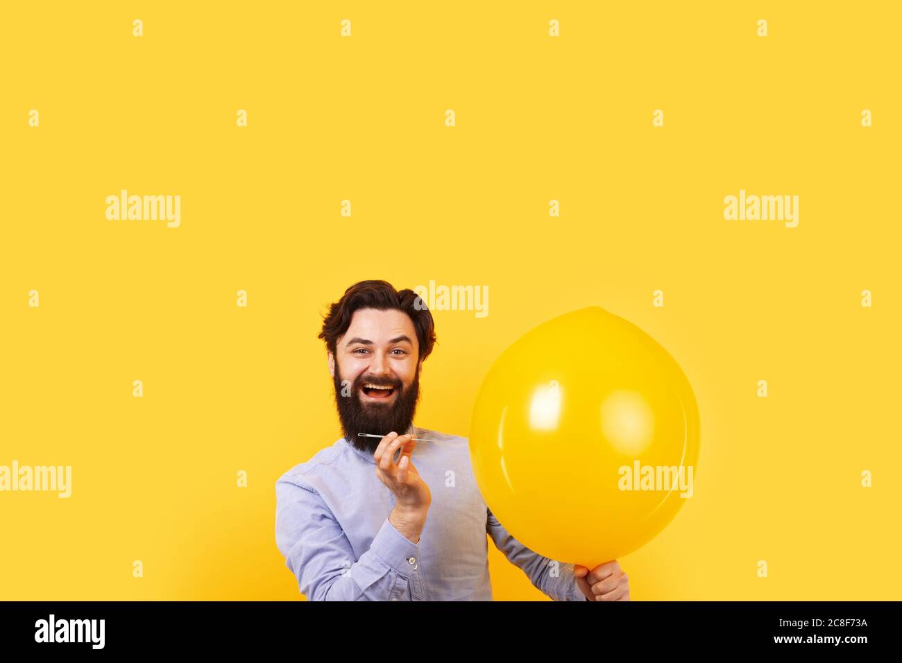 Man holding needle over yellow air balloon, a moment before bubble burst. Stock Photo