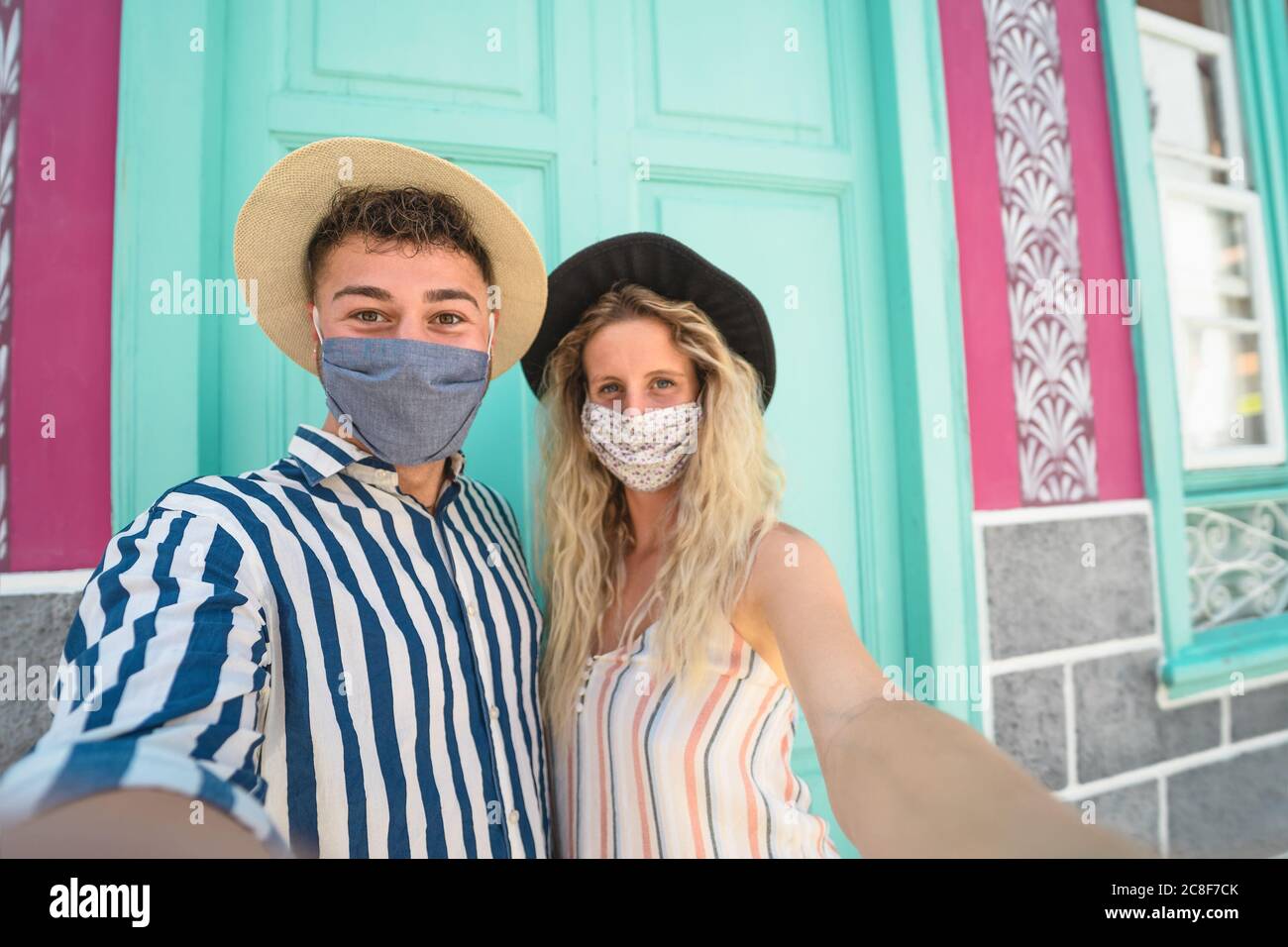 Young couple wearing face mask taking selfie on vacation - People having fun traveling again during corona virus outbreak Stock Photo