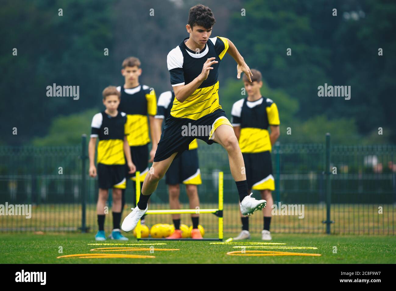 Young Footballer on Training Jumping Over Obstacles. Summer Soccer Camp. Players in a Team Practicing and Improving Speed, Strength and Agility Skills Stock Photo