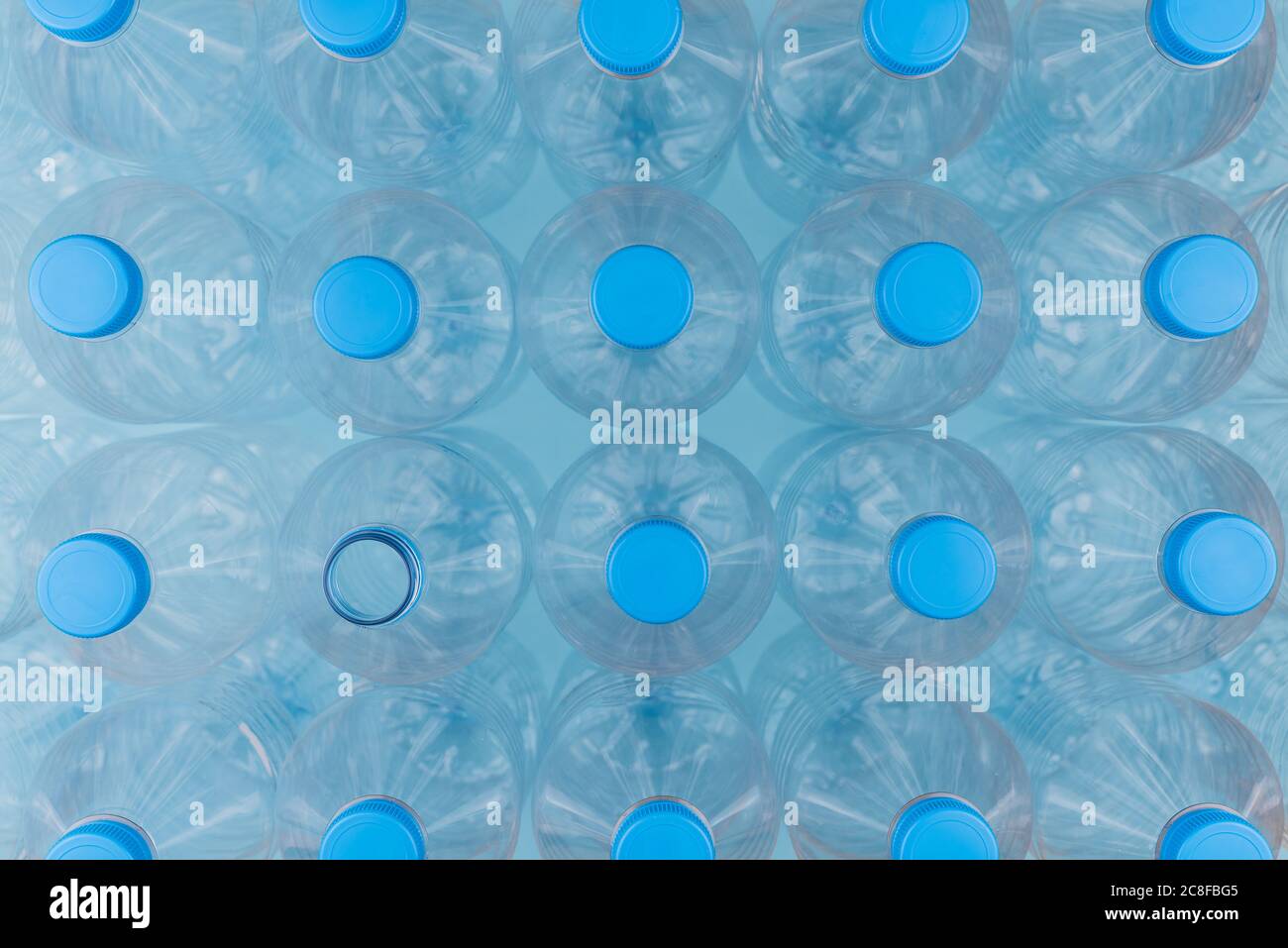 Horizontal color image with an overhead view of an empty clear plastic bottles with caps stacked on a blue background. Recycling and environment conce Stock Photo