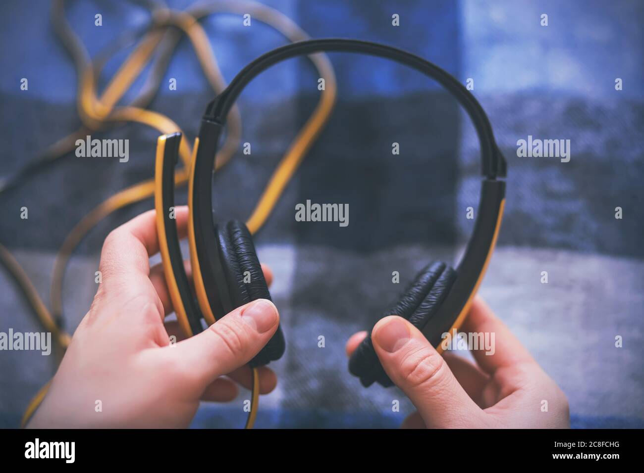 A man is holding large yellow headphones with a long tangled wire and is about to listen to music. Music pause. Stock Photo