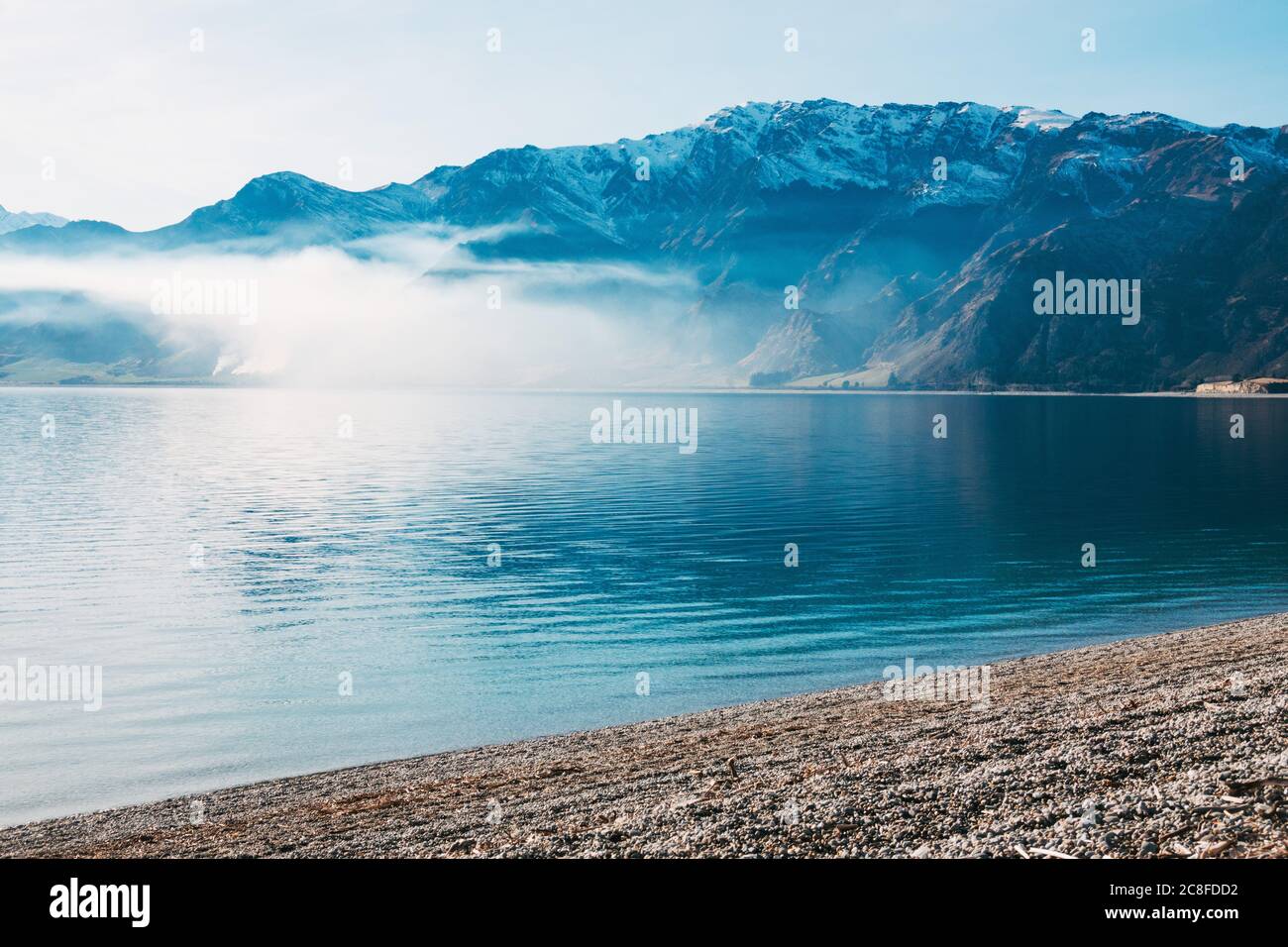 Smoke from a burn off expands across the bay on a perfectly still day at Lake Hawea, New Zealand Stock Photo