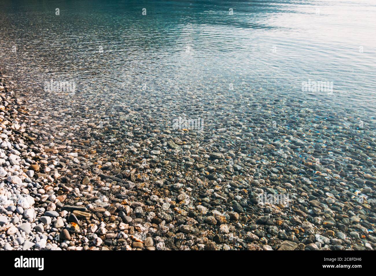 Crystal clear water refracts light as it washes over pebbles on the shore and lakebed of Lake Hawea, New Zealand Stock Photo