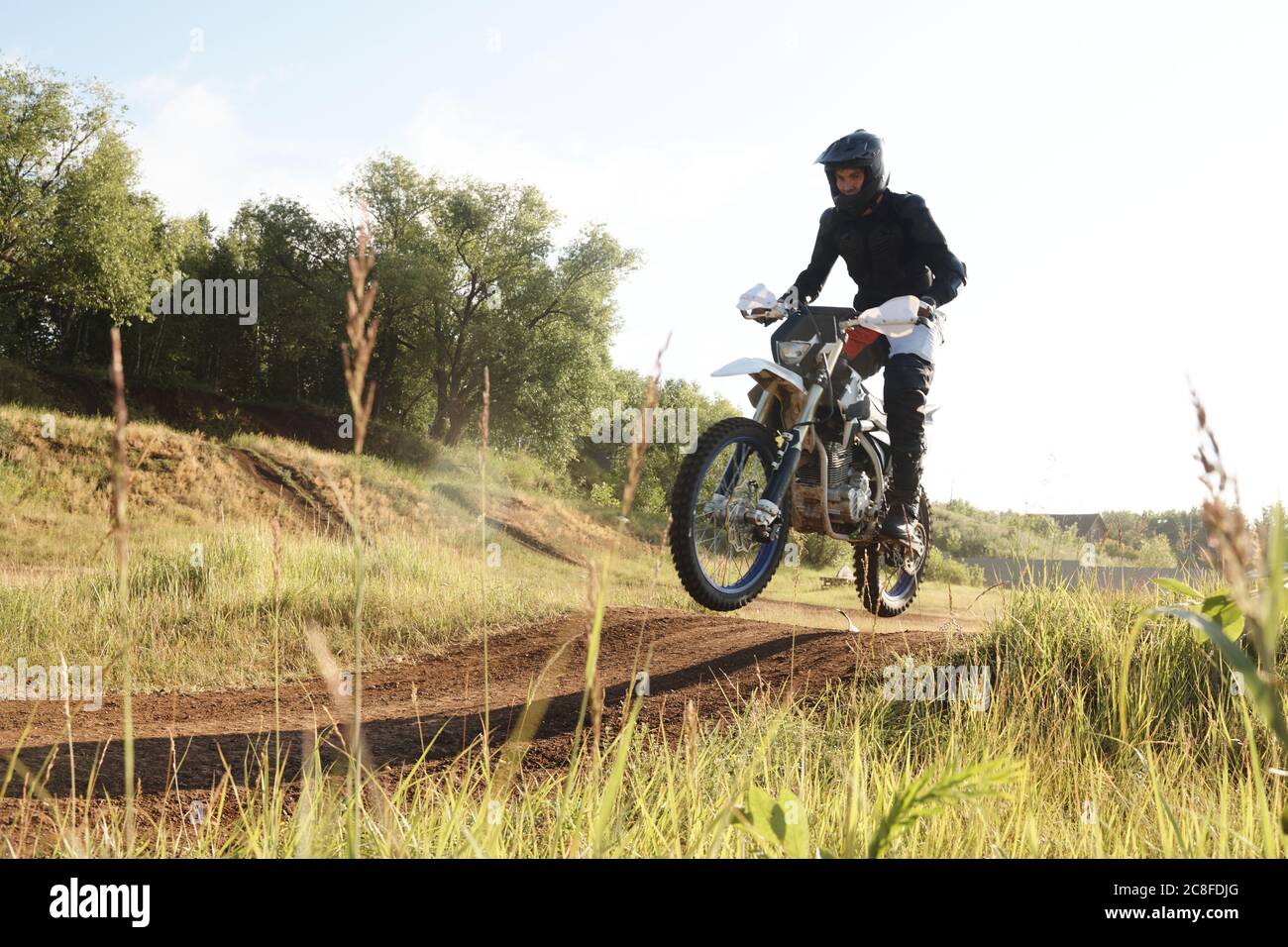 Extreme man in protective wear being in mid air while riding motorbike on hills at competition Stock Photo