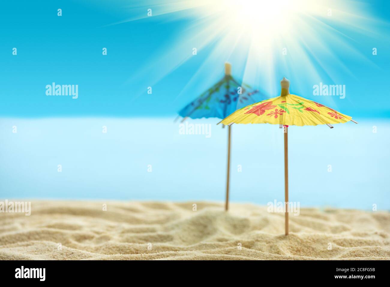 Sun umbrellas on sandy beach with blurry blue ocean, sky and sun beams ...