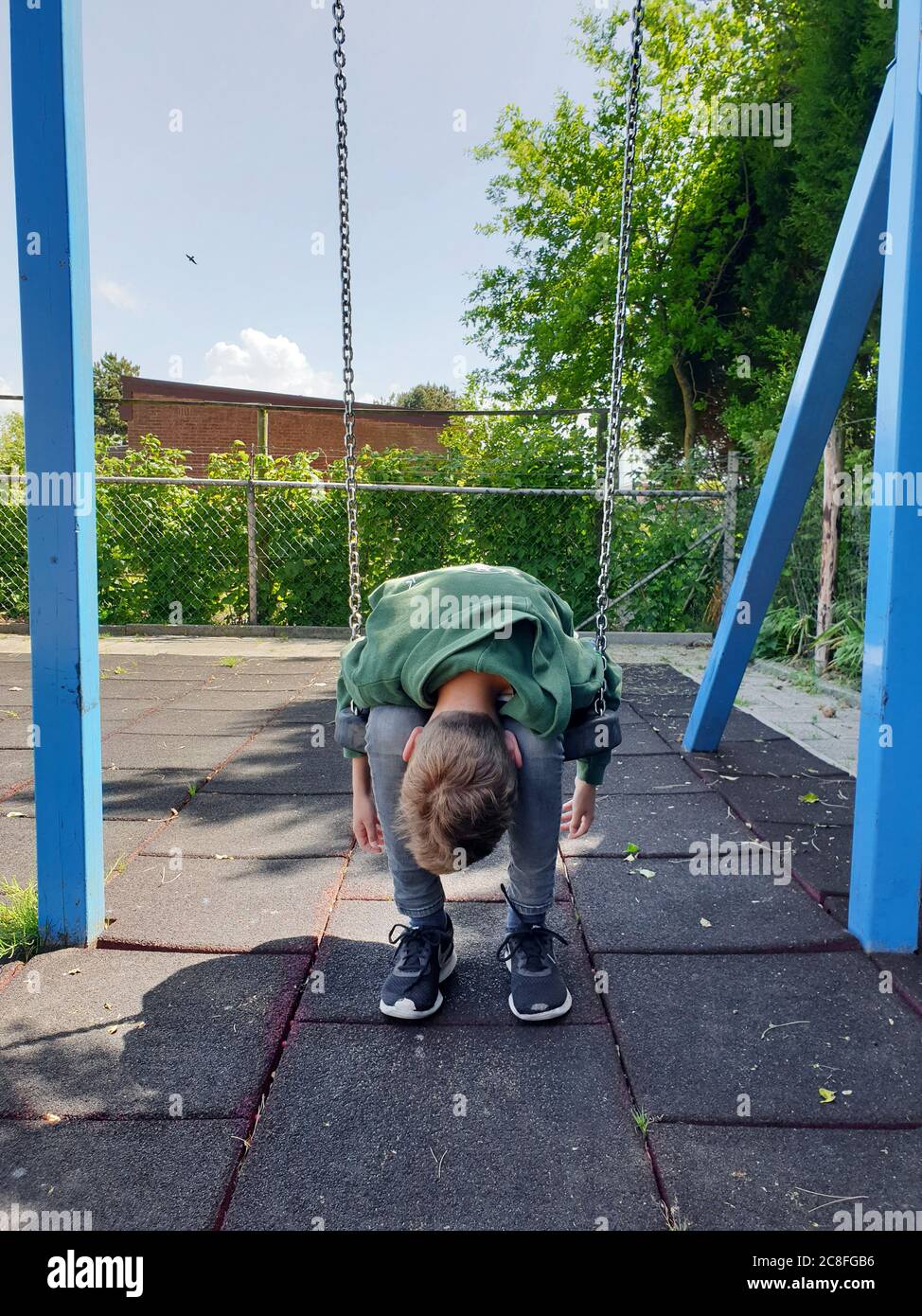 boy sitting listlessly on a swing and has his head hanging, Germany Stock Photo