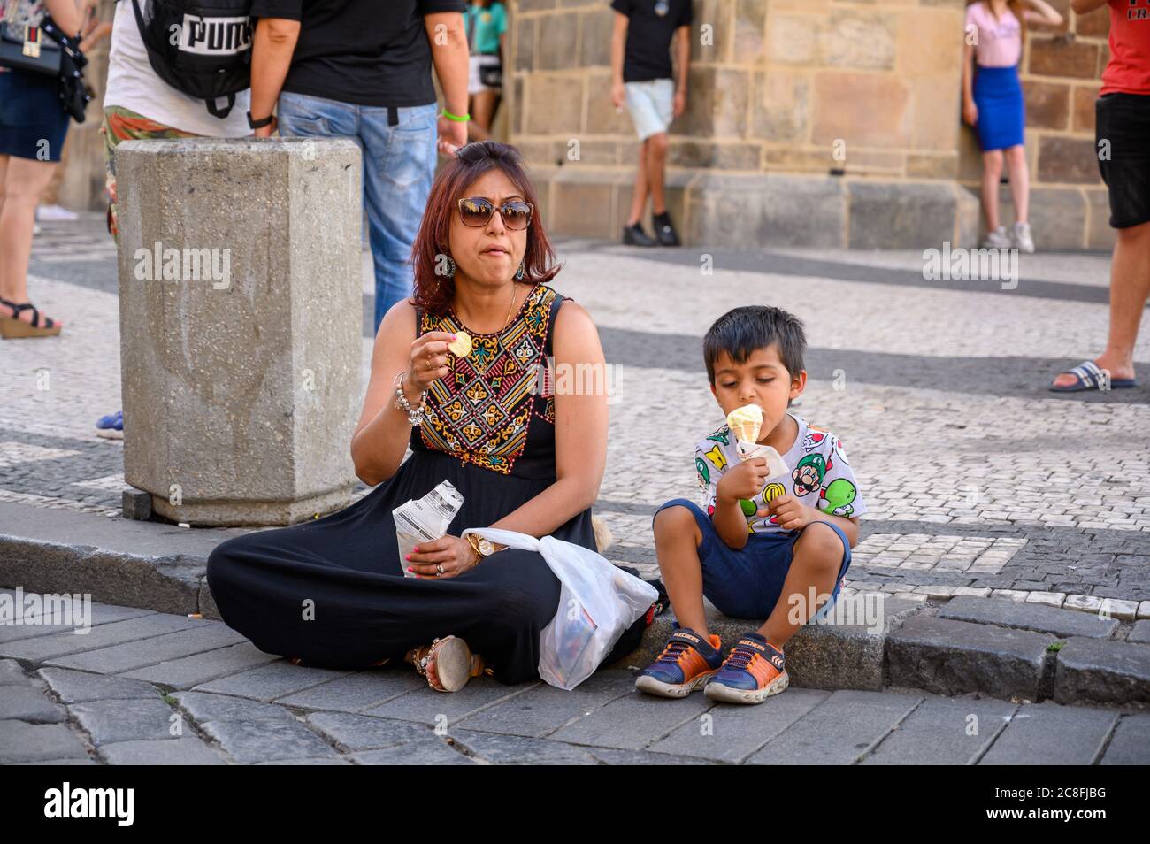 PRAGUE - JULY 20, 2019: A mother and her son sat on a curbside eating snacks Stock Photo