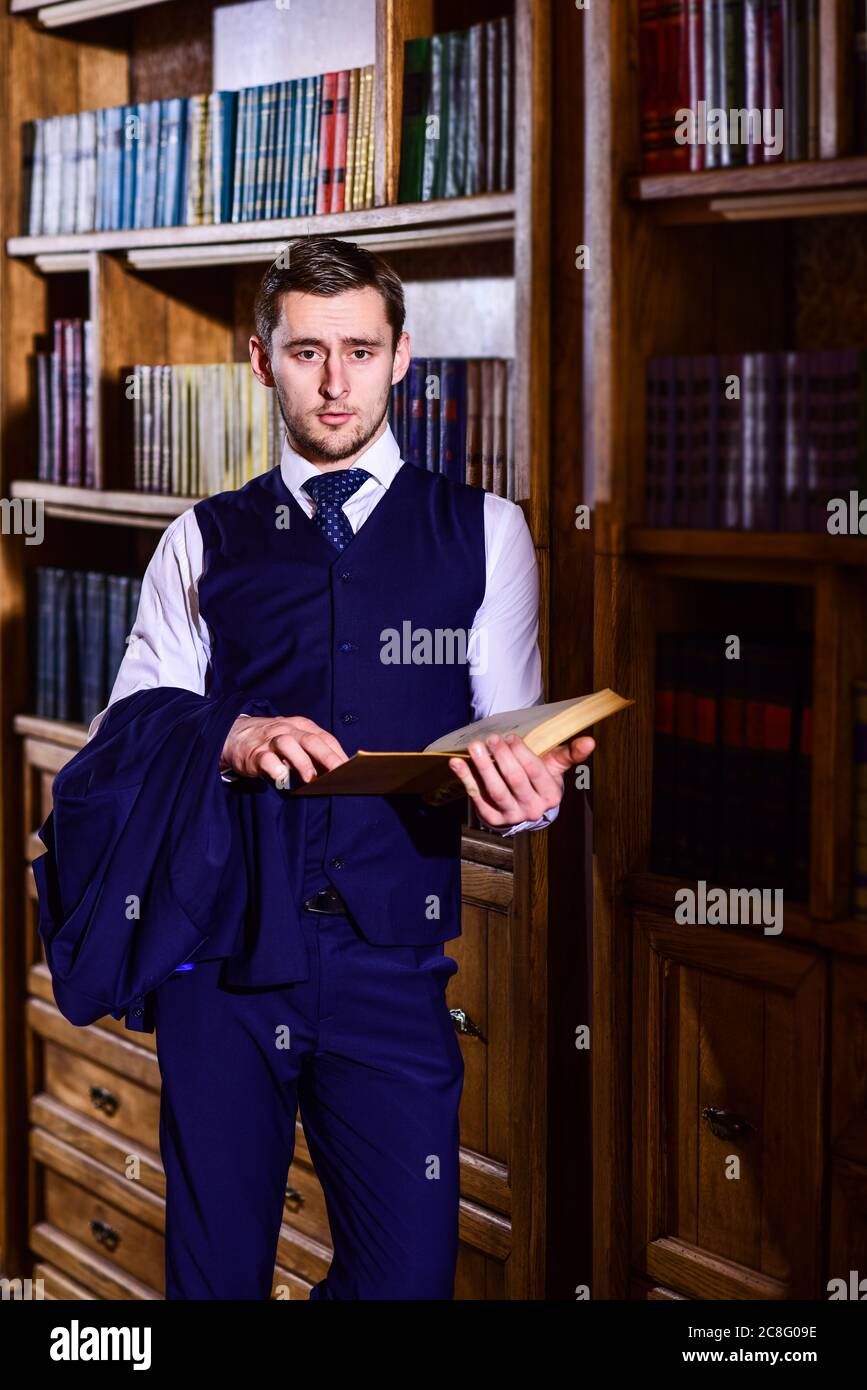 Respectable young man wears classic suit in old library and holds book ...