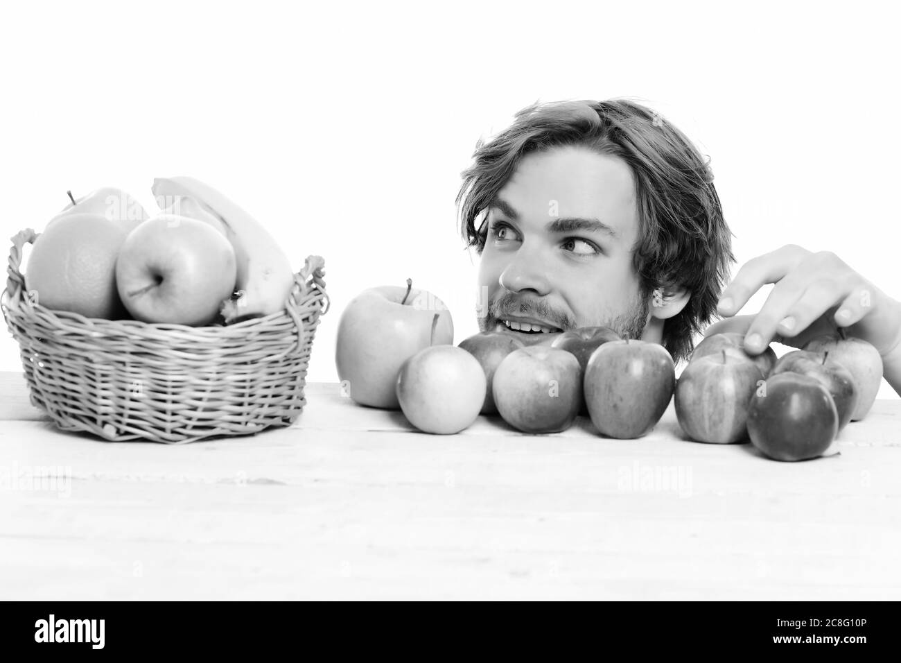 Man stealing apple from wooden table near basket of tropical fruit and green apples on white background Stock Photo