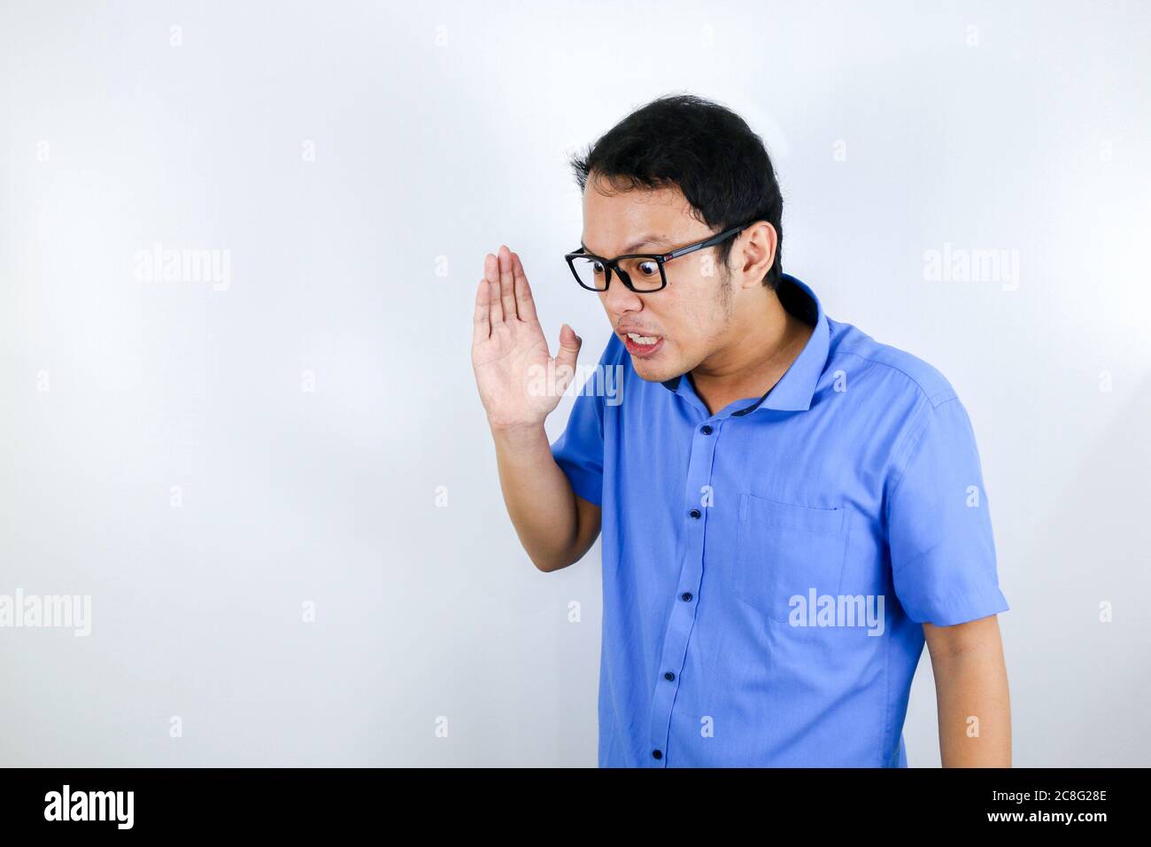 Close up portrait of a young asian man shouting loud and angry facce with arm at his face isolated over white Stock Photo
