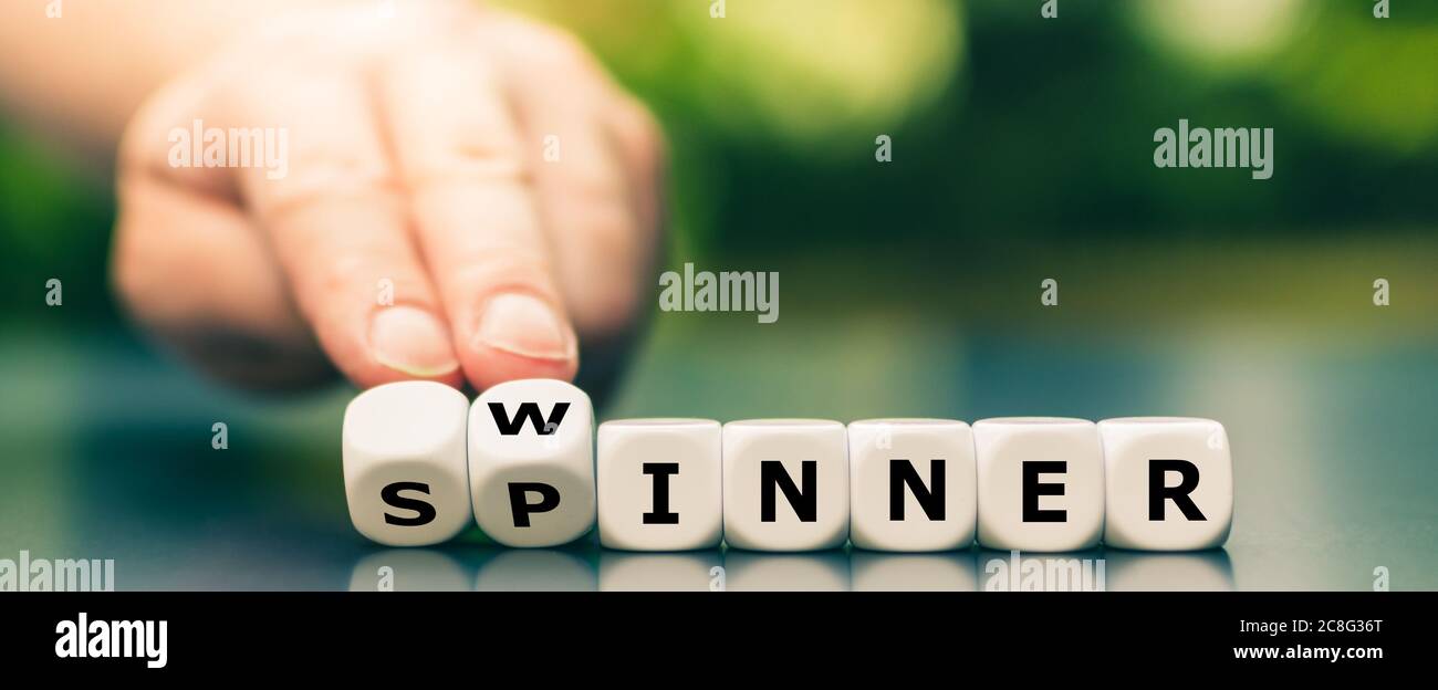 Hand turns dice and changes the word spinner to winner. Stock Photo